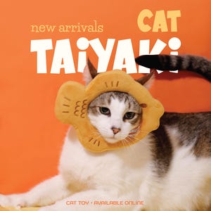 May include: A cat wearing a yellow Taiyaki-shaped cat toy against an orange backdrop. The image features the text "new arrivals CAT TAIYAKI" and "CAT TOY AVAILABLE ONLINE". The cat has white and grey fur.