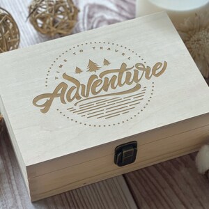 Op de afbeelding: Een houten doos met een scharnierend deksel en een messing sluiting. De doos is versierd met een lasergegraveerd ontwerp dat "Time to Travel Adventure" zegt met een gestileerd lettertype en een cirkel van kleine stippen rond de tekst.