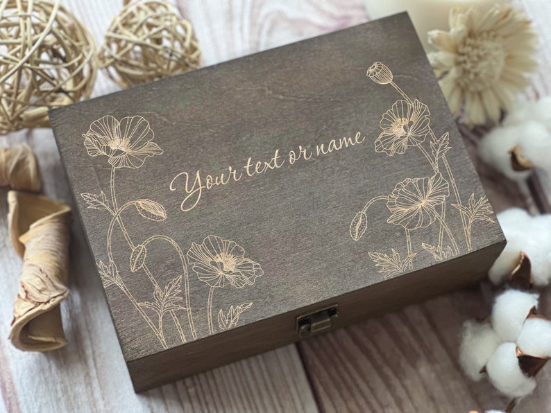 Pu&ograve; includere: Una scatola di legno marrone scuro con un coperchio incernierato e una chiusura in ottone. La scatola &egrave; decorata con un motivo floreale dorato e il testo "Your text or name".
