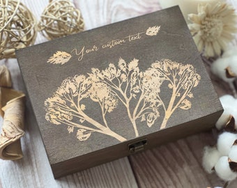 May include: A dark brown wooden box with a hinged lid and a brass latch. The box is decorated with a laser-engraved design of stylised plants in a light brown colour. The text "Your custom text" is engraved on the top of the box.