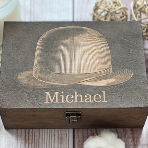 May include: A dark brown wooden box with a hinged lid and a brass latch. The box is engraved with a vintage-style illustration of a hat and the name "Michael".