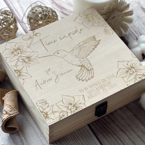 May include: A wooden box with a hummingbird and floral design. The box is engraved with the text "Time capsule for Andrew Johnson to be opened on your 18th birthday August 23, 2038".