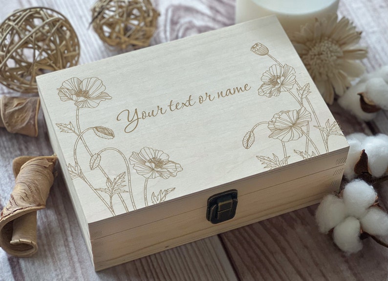 Pu&ograve; includere: Una scatola di legno con un coperchio incernierato e una chiusura a scatto. La scatola &egrave; decorata con un motivo floreale di papaveri e il testo "Your text or name".
