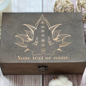 May include: A wooden box with a hinged lid and a latch. The box is decorated with an engraved design of a person sitting in a lotus position with a mandala behind them. The text "Your text or name" is engraved below the design.