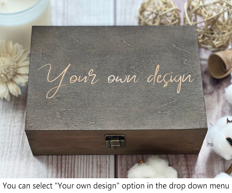 May include: A dark brown wooden box with a hinged lid and a brass latch. The box has the words "Your own design" engraved on the top in a gold color.