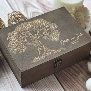 Könnte beinhalten: Eine dunkelbraune Holzkiste mit einem goldenen, gravierten Baumdesign und dem Text "Oliver und Julia 2022".