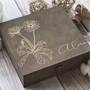 Puede incluir: Una caja de madera marrón oscuro con tapa con bisagras. La caja tiene un diseño floral y la palabra "Aloha" grabada en la parte superior.