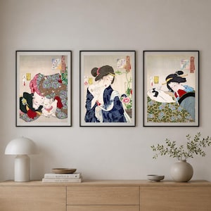 Könnte beinhalten: Drei gerahmte Kunstdrucke mit traditionellen japanischen Illustrationen. Jeder Druck zeigt eine Frau in einem Kimono mit detaillierten Mustern und Farben. Die Drucke werden über einem Holzschrank ausgestellt und schaffen eine zusammenhängende Ästhetik.