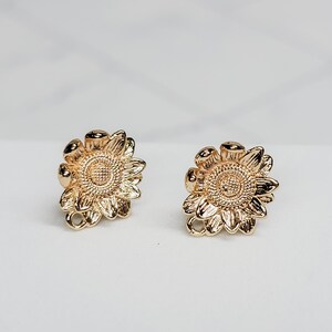 May include: A pair of gold-tone sunflower earrings. The earrings are small and delicate, with a simple design.