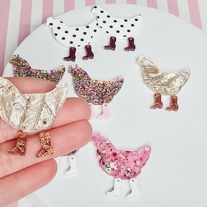 May include: Assortment of colorful chicken shaped resin embellishments with glitter and painted details. Each chicken has a pair of boots. The chickens are in various colors including pink, gold, brown, white, and black.