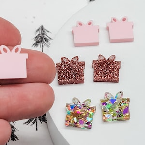 May include: Six pink, brown, and iridescent glitter gift box shaped earrings. The earrings are all different designs and are perfect for adding a festive touch to any outfit.