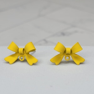 May include: A pair of yellow bow-shaped earrings. The earrings are made of metal and have a simple design.