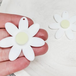 May include: Two white daisy-shaped charms with a yellow center. The charms have a hole at the top for hanging.