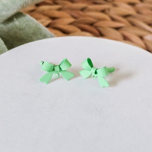 May include: A pair of light green bow earrings. The bows are made of metal and have a shiny finish.