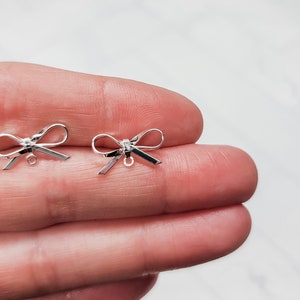 Puede incluir: Dos abalorios de plata en forma de lazo con un bucle para sujetar a joyas u otras manualidades.