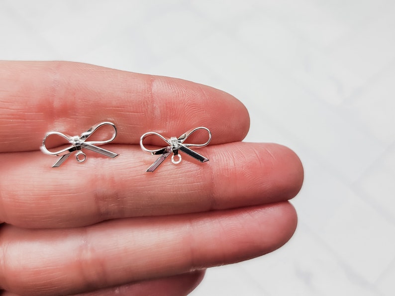 Puede incluir: Dos abalorios de plata en forma de lazo con un bucle para sujetar a joyas u otras manualidades.