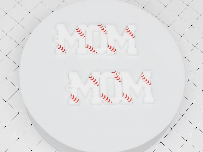 May include: Two white acrylic "MOM" signs with a baseball pattern. The letters are outlined in red.