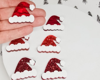 May include: Red glitter Santa hat ornaments with white trim and a small white pom-pom. The ornaments are in the shape of Santa hats and are a festive holiday decoration. Several ornaments are visible.