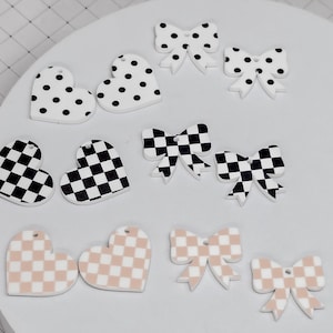 May include: A collection of decorative heart and bow-shaped charms. The charms feature various patterns, including black and white polka dots, black and white checkerboard, and a tan and white checkerboard design. These charms are ideal for crafting.