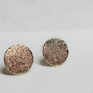 May include: A pair of gold-toned earrings with a textured circular design. Each earring has a small hole in the center.