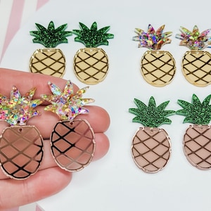 May include: Assortment of six pineapple-shaped earrings with glitter accents. The earrings are available in gold, rose gold, and green glitter finishes.