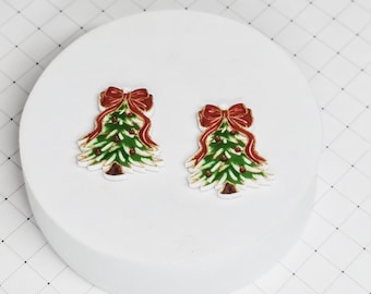 May include: Two Christmas tree ornaments with a green tree, red bow, and gold accents.