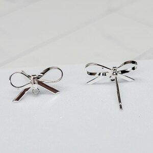 Puede incluir: Dos hallazgos de pendientes en forma de lazo de plata con un bucle para sujetar un dije o una perla.