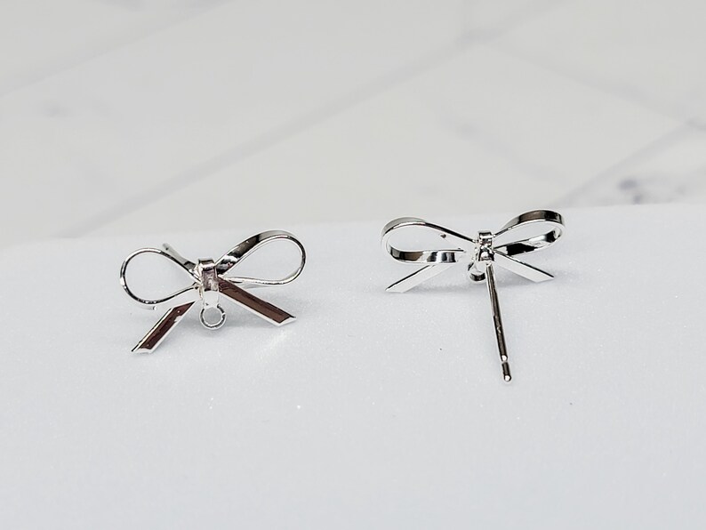 Puede incluir: Dos hallazgos de pendientes en forma de lazo de plata con un bucle para sujetar un dije o una perla.