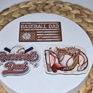 May include: Three baseball-themed stickers with the text "Baseball Dad" on a white background. The stickers are brown, red, white, and blue.