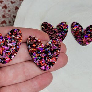 May include: Three red, pink, and iridescent glitter heart-shaped resin embellishments.