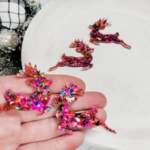 May include: Four pink and iridescent glitter reindeer ornaments. The reindeer are in a leaping pose with their antlers raised.