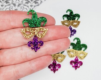 May include: Assortment of Mardi Gras themed glitter embellishments.  The embellishments include a green and gold jester hat, a gold mask, and a purple fleur-de-lis.