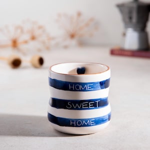 Könnte beinhalten: Weiße Keramiktasse mit blauen Streifen und den Worten "Home Sweet Home" in Schwarz. Die Tasse hat eine Herzform im Inneren.