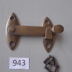 Könnte beinhalten: Türverschluss aus Messing mit einem Hebelgriff und zwei Montageplatten. Der Verschluss wird mit einer kleinen Tüte Schrauben geliefert. Die Nummer 943 ist auf einem weißen Papierstück geschrieben.