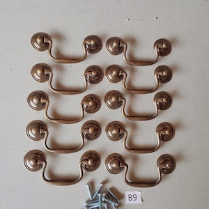 May include: A set of ten antique-style bronze drawer pulls with matching screws. Each pull features a circular backplate and a curved handle. The hardware is designed for furniture restoration or new builds.