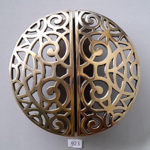 May include: A pair of ornate brass door handles with a circular, intricate design. The handles are separated by a thin vertical line.