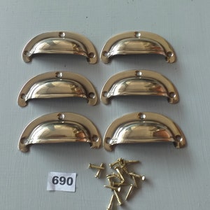 May include: Six gold-toned metal cabinet pulls with a rounded, curved shape. The pulls are arranged in two rows of three. A small pile of gold-toned screws is in the lower right corner of the image. The number 690 is printed on a white label in the lower left corner of the image.