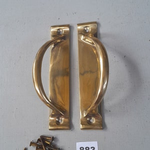 May include: Two gold-toned door handles with a curved design and a set of screws. The handles are rectangular and have a polished finish. The number 883 is written on a white label.