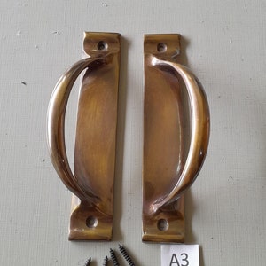 May include: Two antique brass door handles with a curved design and four screws. The handles are on a light gray surface with the text "A3" written on a white label.