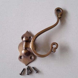 May include: A brass-toned wall hook with an ornate backplate and a curved hook. It comes with four black screws for installation. A small white label displays the number "987".