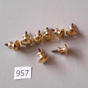 May include: Nine gold-toned cabinet knobs with screws. The knobs are round with a raised center and a slightly flared base. The screws are brown.