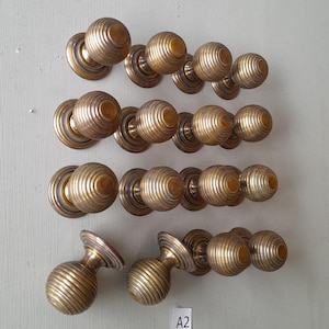May include: A set of 18 antique brass door knobs with a ribbed design. The knobs are arranged in three rows of six. The knobs are all in good condition and have a nice patina.