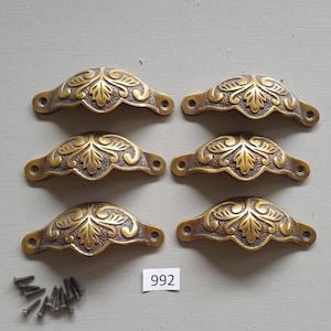 May include: Six antique brass drawer pulls with a floral design. The pulls are arranged in two rows of three. Each pull has two screw holes. The pulls are on a white background. The number 992 is written on a white tag.