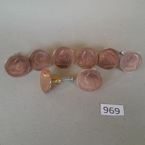 May include: Eight copper-colored coin-shaped drawer pulls with a gold-colored knob and screw. The pulls are arranged in a semi-circle with the knob in the center. The number 969 is written on a white label.