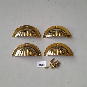 May include: Four gold-toned shell-shaped cabinet pulls with a fluted design. The pulls are arranged in two rows of two. A small pile of gold-toned screws is included. The number 840 is written on a white label.