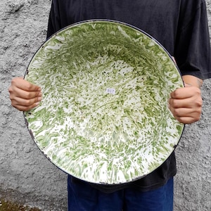 May include: Large, round enamelware bowl with a green and white marbled pattern. The bowl has a black rim and a small white tag with the number "B17". This vintage-style bowl is ideal for serving or display.