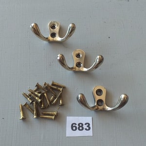 May include: Three silver double hooks with a pile of gold screws. The number 683 is written on a white piece of paper.