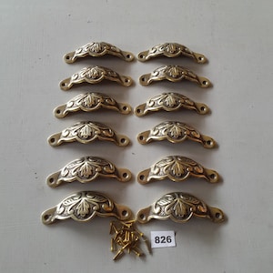 May include: Ten ornate brass drawer pulls with a leaf design. The pulls are arranged in two rows of five. A small bag of screws is included. The number 826 is written on a white tag.