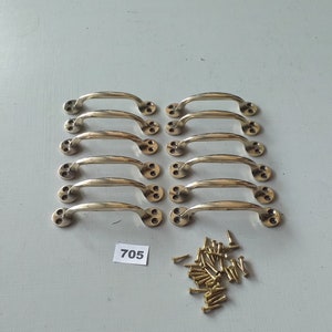 May include: Ten gold-toned cabinet door pulls with a simple, curved design. The pulls are arranged in two rows of five. A pile of gold-toned screws is below the pulls. A white label with the number 705 is in the lower left corner of the image.
