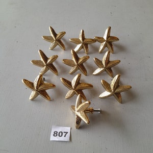 May include: Twelve gold starfish drawer pulls with a textured surface. The pulls are arranged in a semi-circle on a white surface. The number 807 is written on a white tag.
